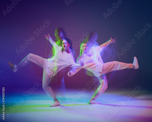 Portrait of young girls, friends dancing hip-hop isolated over gradient blue purple background in neon with mixed light.