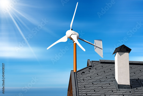 Close-up of a small wind turbine on the top of a roof of a house, against a blue sky with clouds and sunbeams. Renewable energy concept. photo