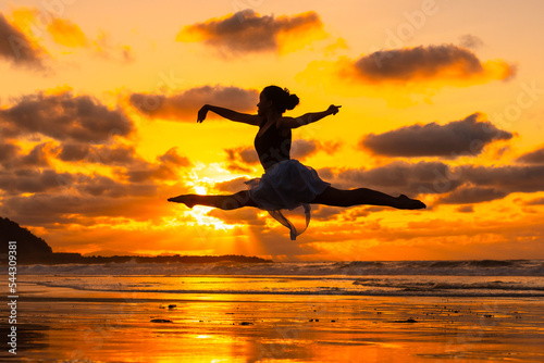 Young dancer on the beach at sunset performing a jump with the sea in the background