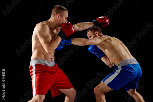 Fight. Dynamic portrait of two professional boxer in sports uniform boxing isolated on dark background. Concept of sport, competition, training, energy. © master1305