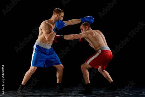 Fight. Dynamic portrait of two professional boxer in sports uniform boxing isolated on dark background. Concept of sport, competition, training, energy. © master1305