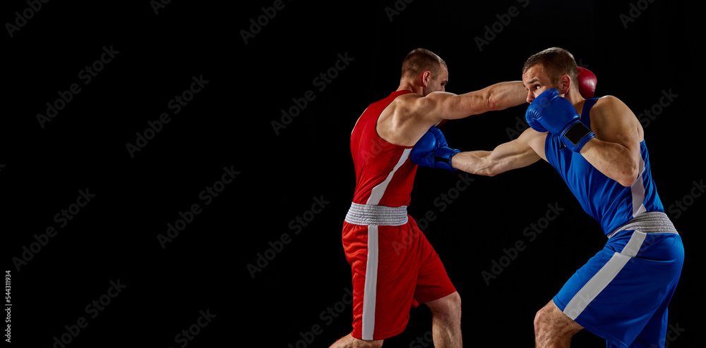 Male professional boxers in blue and red sports uniform practicing punch isolated on dark background. Concept of sport, competition, training, energy.