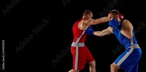 Male professional boxers in blue and red sports uniform practicing punch isolated on dark background. Concept of sport, competition, training, energy.