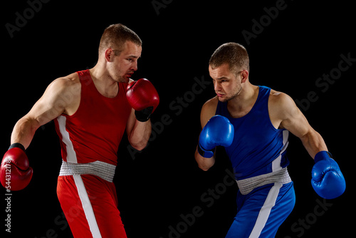 Male professional boxers in blue and red sports uniform practicing punch isolated on dark background. Concept of sport, competition, training, energy. © master1305