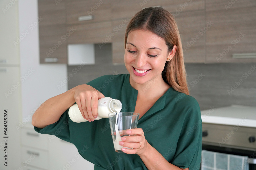 Portrait of young beautiful woman fills the glass with kefir at home Portrait of young beautiful woman fills the glass with kefir at home