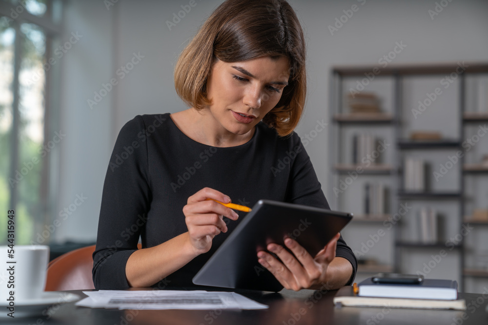 Pensive businesswoman in formal wear working with tablet holding pen Pensive businesswoman in formal wear working with tablet holding pen