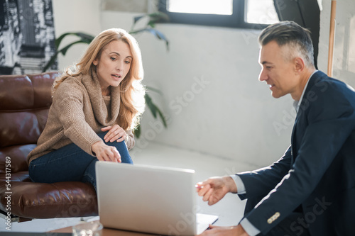 Blonde woman and a mid aged manlooking at something on a laptop and discussing