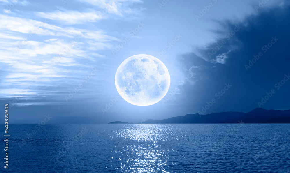 Night sky with blue moon in the clouds over the calm blue sea 