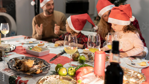 Caucasian family of four with Santa hats celebrating Christmas dinner. Focus on candle