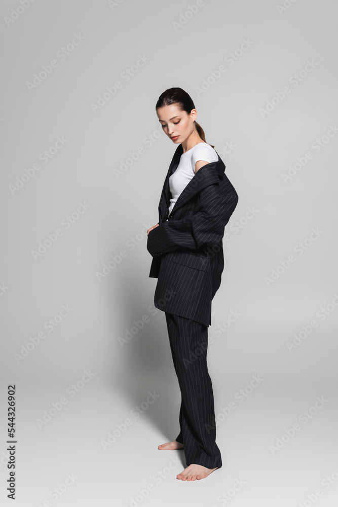 Barefoot model in black suit standing on grey background with shadow. Barefoot model in black suit standing on grey background with shadow.