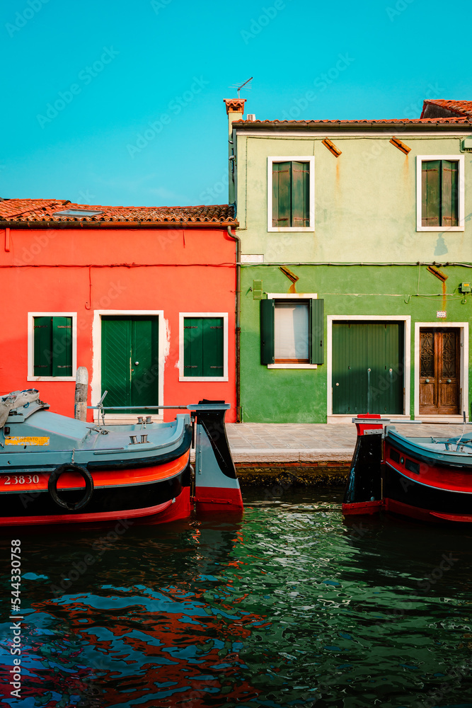 Burano dwellings in front of canal with moored boats, vertical