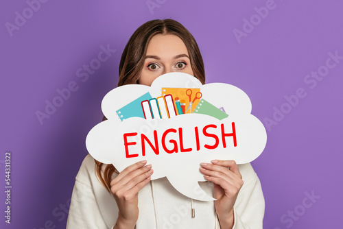 young shocked woman holding blank speech bubble with text learn english isolated on purple background