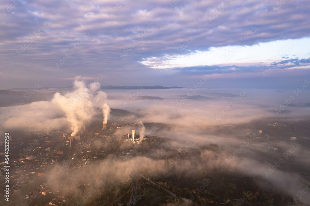 Aerial view of foggy morning in a industrial city, with steam coming off the furnaces and cooling towers. Old metallurgic factories in Resita city, Romania.