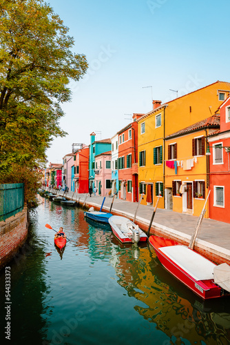 Characteristic Burano street with canal and canoes of tourists and colorful houses at sunset