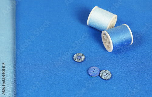 Blue background with spools of thread and buttons. Accessories for sewing.