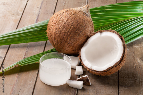 refined coconut oil with old coconuts and leaves on wooden background.