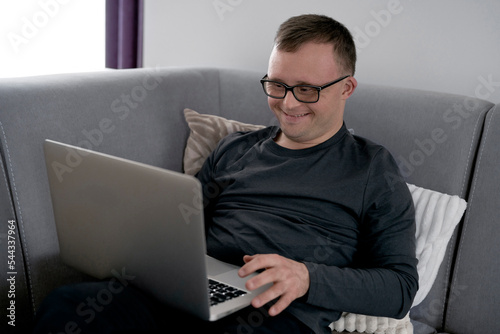 Man with down syndrome using laptop at home while sitting on sofa