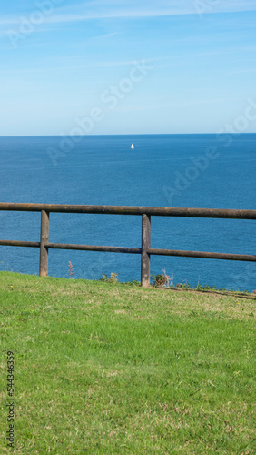 Fototapeta Naklejka Na Ścianę i Meble -  Barco blanco distante en horizonte marino y valla de madera en ladera verde