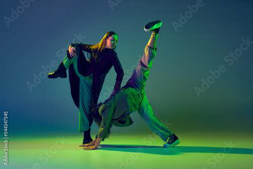 Two dancers, stylish fashionable dance couple dancing contemporary dance on colorful gradient blue-green background in neon light. Concept of art, creativity, movement, style and fashion, action.