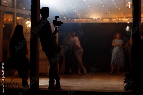 Fotografie Silhouette of cameraman standing with video action film production digital camera at wedding, birthday party