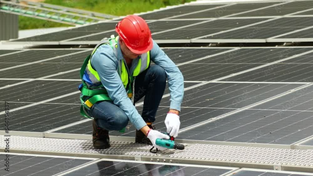 Hispanic male electrician engineer in safety hardhat helmet using electric drill for installation and maintaining solar cell panels on factory building rooftop. clean and green alternative energy Hispanic male electrician engineer in safety hardhat helmet using electric drill for installation and maintaining solar cell panels on factory building rooftop. clean and green alternative energy
