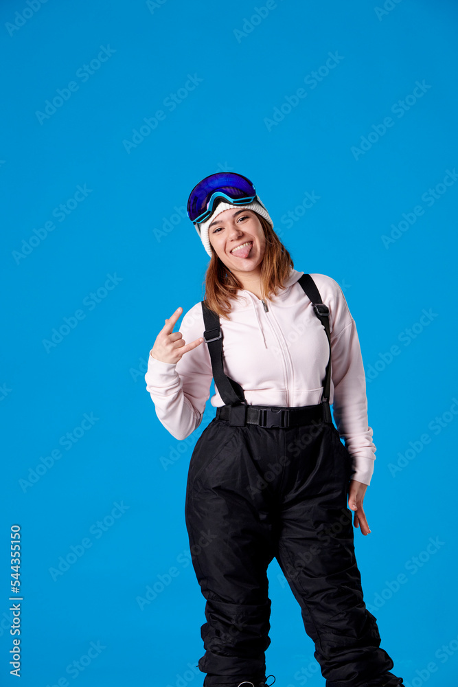 woman in snowboard clothes sticking out her tongue and making the horns with her hand woman in snowboard clothes sticking out her tongue and making the horns with her hand