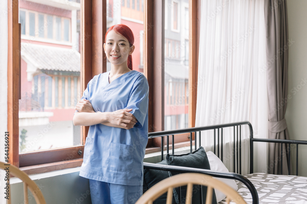 Fototapeta premium Portrait of Asian therapist woman nurse wearing medical scrubs in the house of patient. Caregiver visit at home. Home health care and nursing home concept.