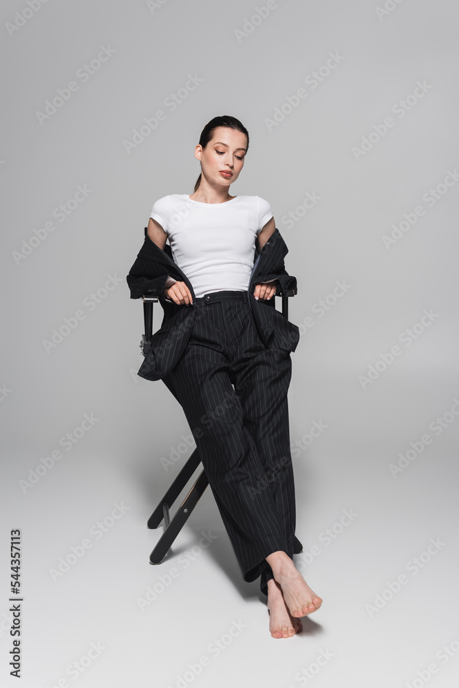 Stylish woman in white t-shirt and striped suit sitting on folding chair on grey background. Stylish woman in white t-shirt and striped suit sitting on folding chair on grey background.