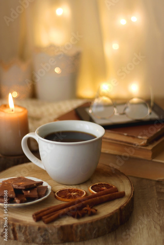 Bowl of cookies  cup of tea or coffee  chocolate  spices  knitted blanket  books  glasses and candle on the table. Cozy hygge atmosphere at home. Selective focus.