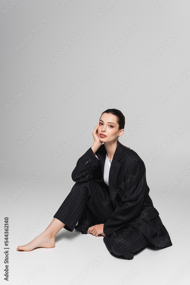 Stylish barefoot model in suit sitting on grey background. Stylish barefoot model in suit sitting on grey background.