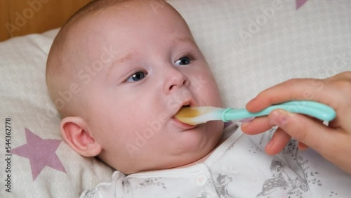 Video of mom feeding baby boy on the bed. Mother trying to feed little baby with fruit or vegetable mash. Little cute baby boy eating first food from spoon. Complementary feeding infant at home. 4k