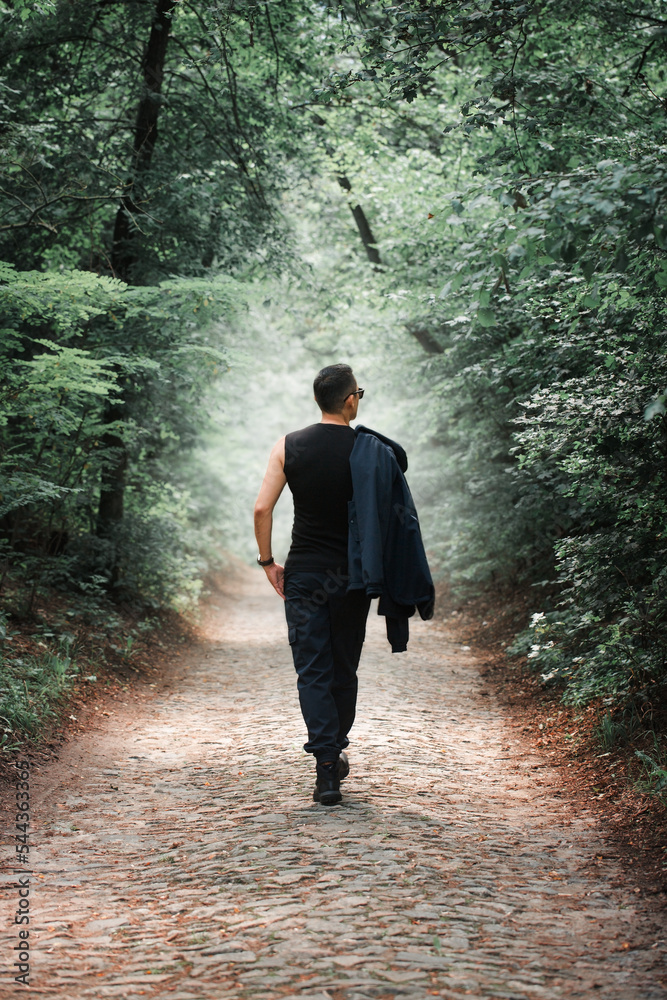 a man in black walks on the cobblestones in the foggy forest, back view