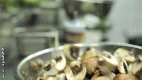 Chef mixing chopped mushrooms with spices in metal bowl in restaurant kitchen, close up photo