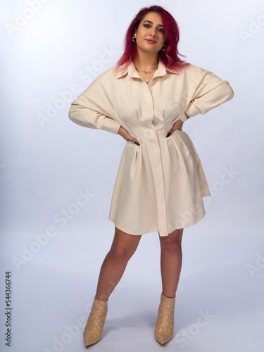 A young girl with long brown hair and brown eyes on a white background. She is wearing a short beige dress, high-heeled ankle boots. Full height