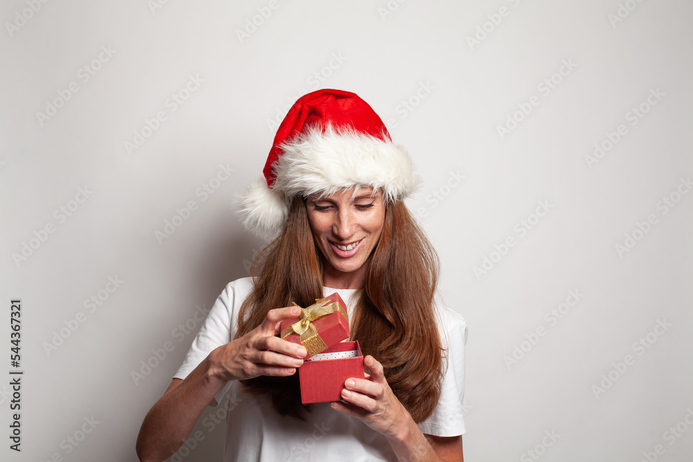 Joyful beautiful smiling woman in red Santa Christmas hat opening red gift on white background Joyful beautiful smiling woman in red Santa Christmas hat opening red gift on white background