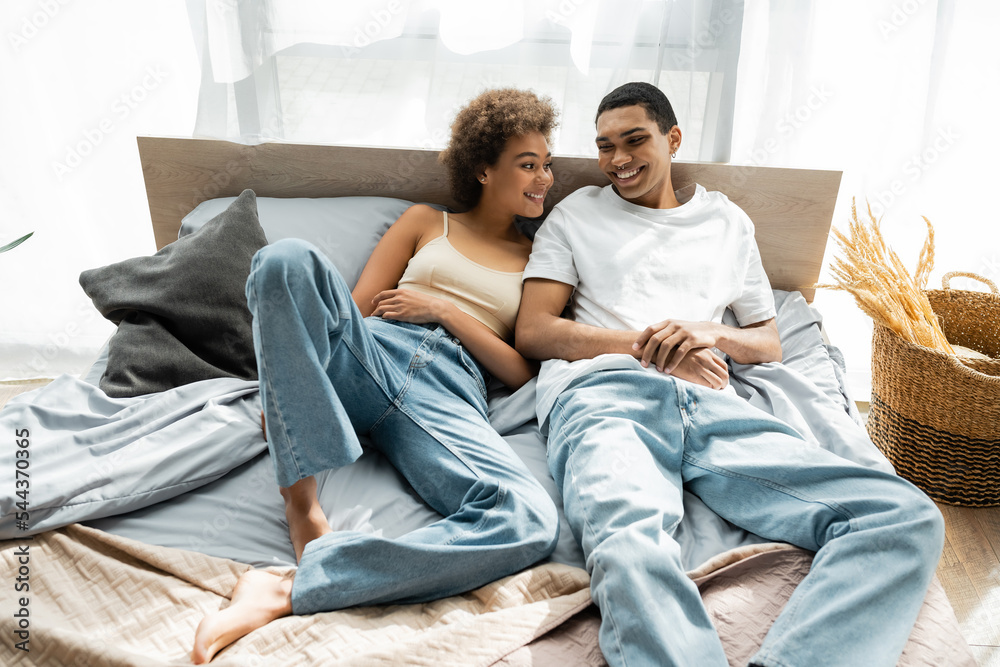 young african american couple in jeans smiling while lying on bed. young african american couple in jeans smiling while lying on bed.