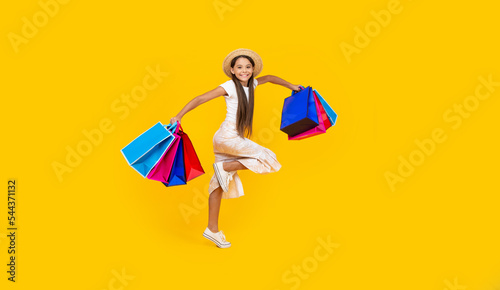 happy teen girl running with shopping bags on yellow background. full length