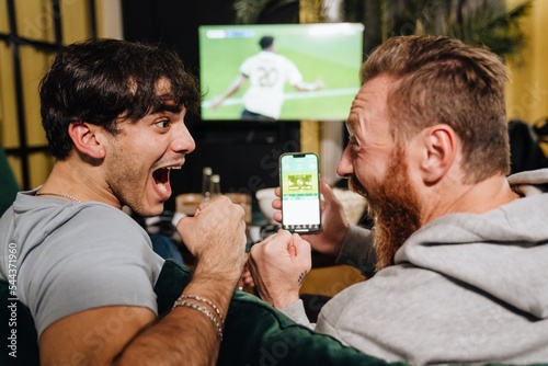 Foto Two men watching football match and making bets at bookmaker's website in front