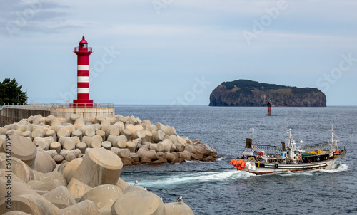 Red and white small lighthouse and mountain view along the rocky coast shoreline of Ulleungdo Island harbor in South Korea photo