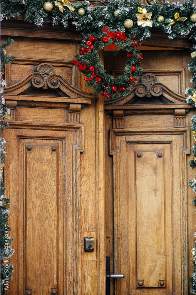 Stylish christmas wreath and fir branches on old wooden doors in building. Modern christmas decor in city street. Winter holidays in Europe. Merry Christmas Stylish christmas wreath and fir branches on old wooden doors in building. Modern christmas decor in city street. Winter holidays in Europe. Merry Christmas
