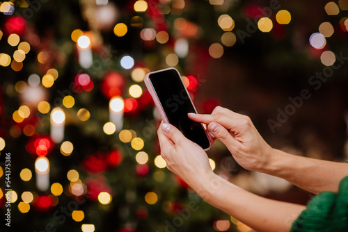 Woman's hands hold smartphone against Christmas tree background. Copy space.