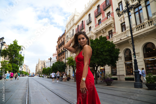 beautiful young woman in a red silk dress posing for a photo session in the avenue of the constitution in seville. The photo is taken from below. Fashion and beauty concept. photo
