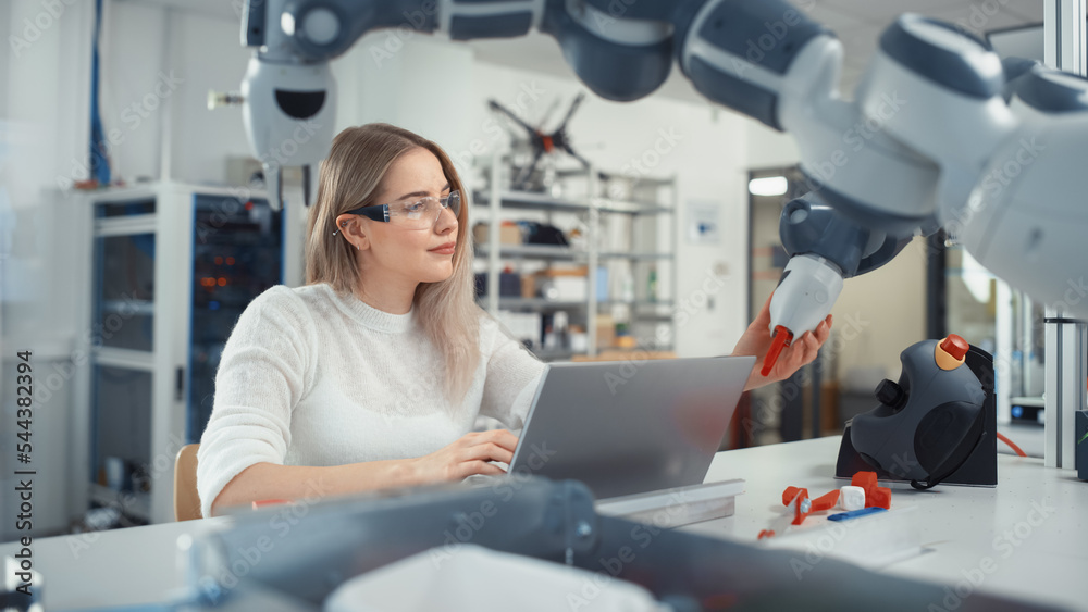 Female Automation Engineer Writes Code on Laptop and Moves Bionic Claw At the Factory. Modern and Futuristic Robotic Equipment Starts the New Era in Computer Science, Machine Learning. Female Automation Engineer Writes Code on Laptop and Moves Bionic Claw At the Factory. Modern and Futuristic Robotic Equipment Starts the New Era in Computer Science, Machine Learning.
