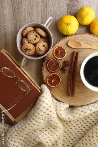 Cup of tea or coffee, various spices, bowl of cookies, tangerines, books, reading glasses and knitted blanket on wooden table. Hygge at home concept, flat lay. © jelena990