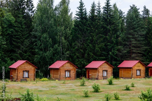 Small wooden log cabins are hardly standing against the backdrop of a coniferous forest.