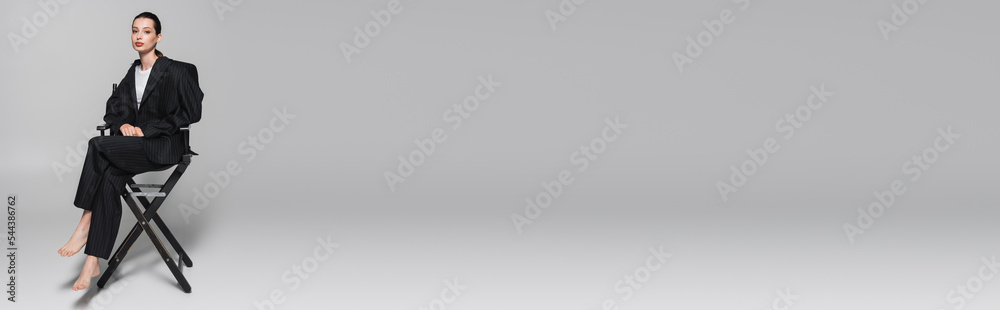 Trendy woman in black suit sitting on folding chair on grey background, banner. Trendy woman in black suit sitting on folding chair on grey background, banner.