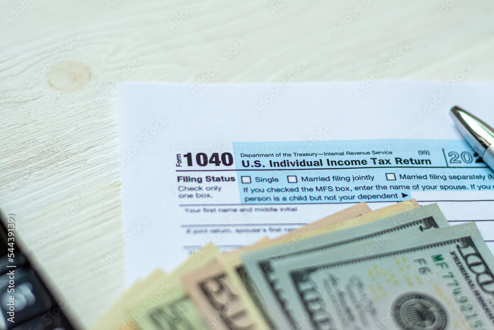 Obraz premium U.S. individual income tax return on a wooden table next to a calculator, dollars, money, a pen and a notepad. Blank US tax forms.