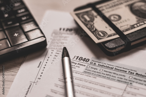 U.S. individual and corporation income tax return close-up next to a calculator  dollars  money  a pen and a notepad on a wooden table. Retro old style photo.