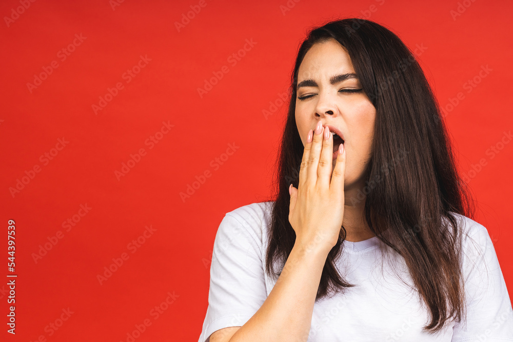 Portrait of a young cute tired woman yawning with her eyes closed and covering her mouth, isolated over red background. Portrait of a young cute tired woman yawning with her eyes closed and covering her mouth, isolated over red background.