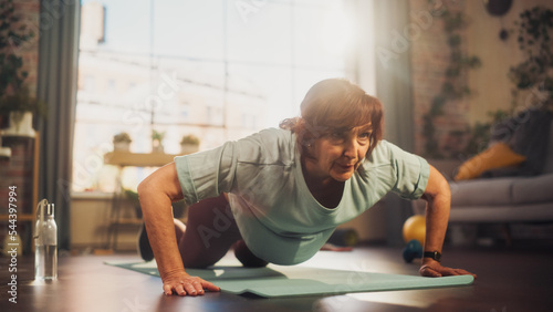Bild auf Leinwand Happy Fit Senior Woman Training on a Yoga Mat, Doing Burpees Exercises During Morning Workout at Home in Sunny Apartment
